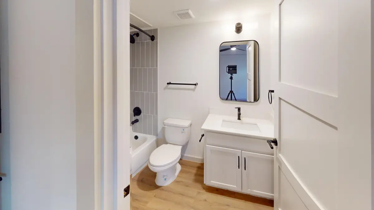 Bathroom with a white vanity, quartz-style, black-framed mirror, and a gray vertical-tile tub-and-shower