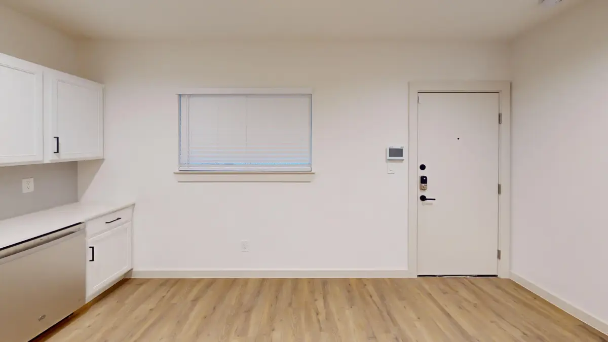 Studio-style living space with a kitchenette, a blinded window, and an entry door with a keypad smart lock