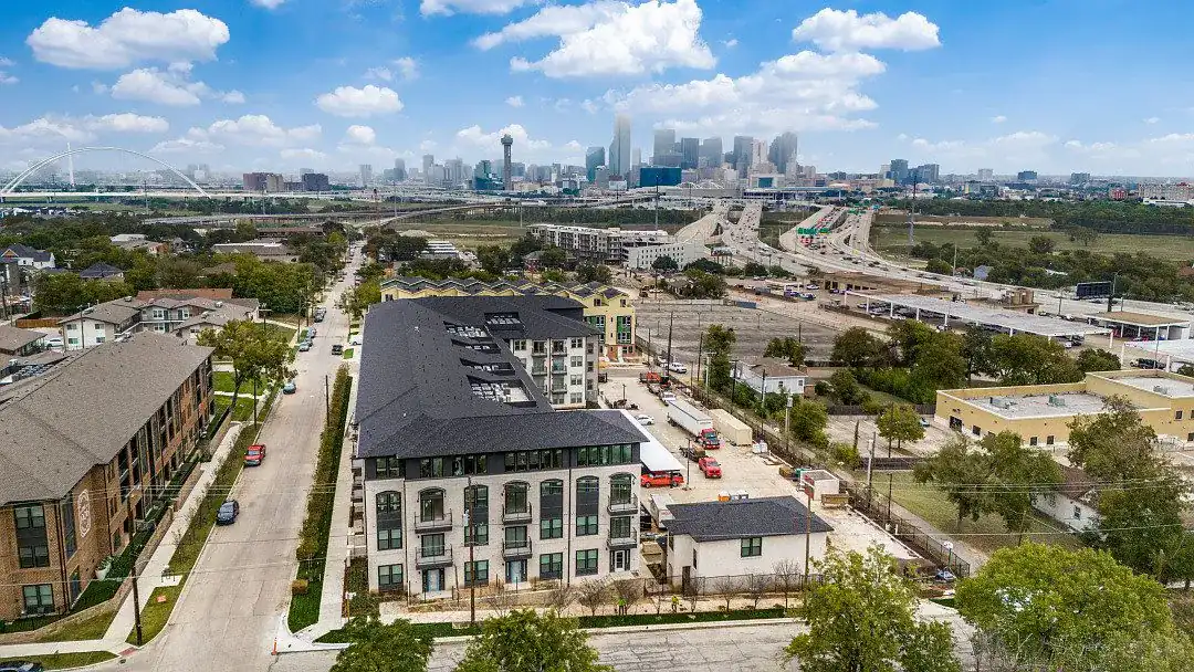 Aerial view of the four-story Burnett Lofts building among the Oak Cliff streets, with the downtown Dallas skyline on the horizon