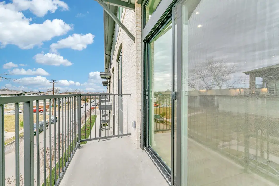 Concrete balcony with dark metal picket railing, a full-height sliding glass door and street views past cream brick