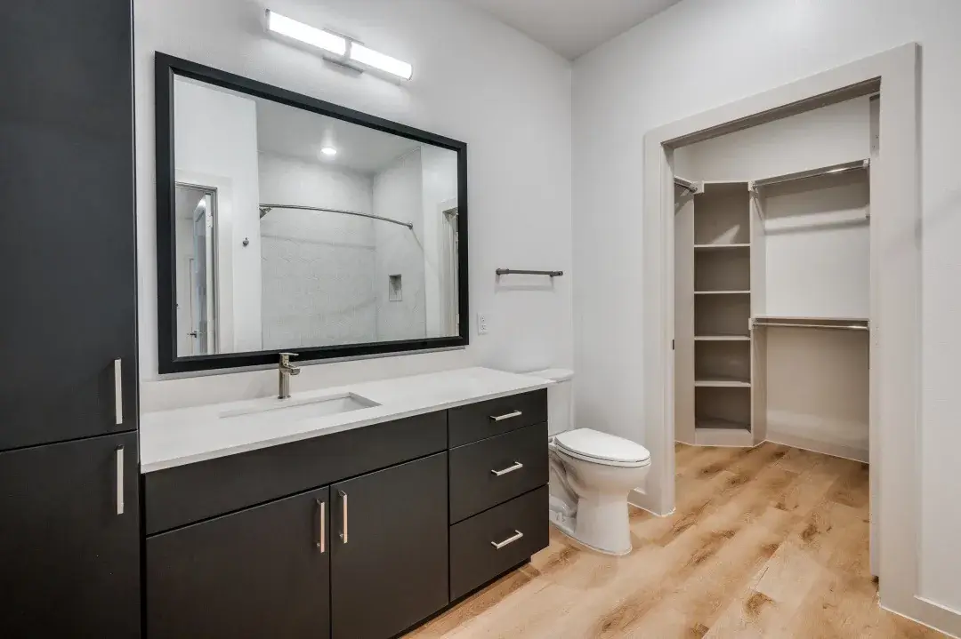 Bathroom with dark-cabinet quartz vanity, black-framed mirror and an open walk-in closet with built-in shelving