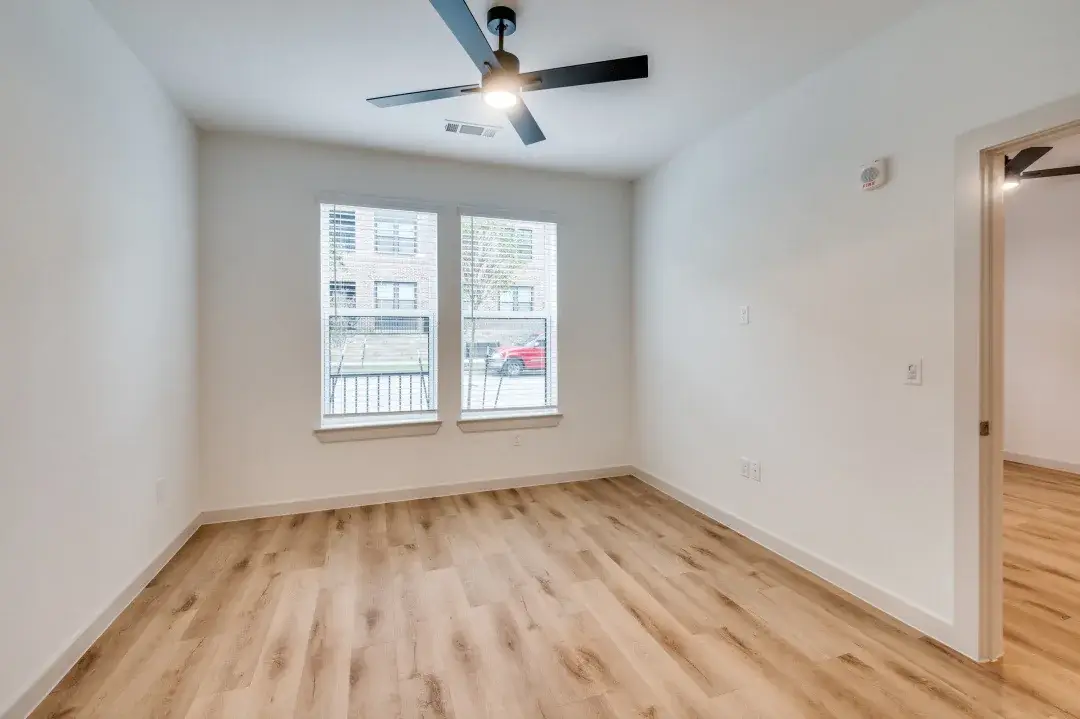 Bedroom with paired street-facing windows, a matte black ceiling fan and light wood-style flooring