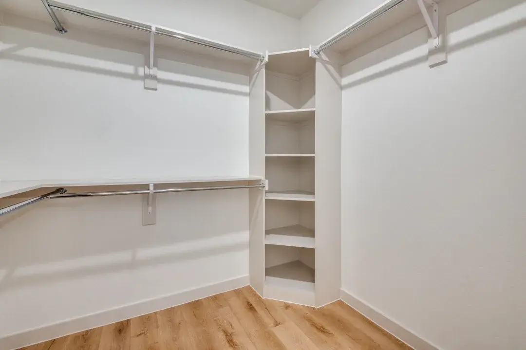 Corner walk-in closet with chrome double hanging rods, a built-in shelf tower and wood-style flooring