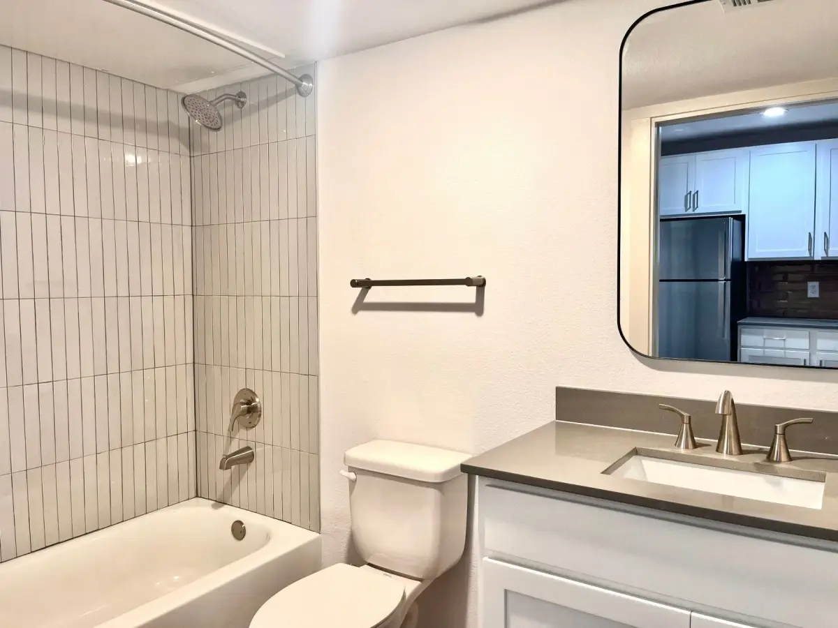 Bathroom with a white vanity, solid surface top, a framed mirror, and a white vertical-tile tub-and-shower