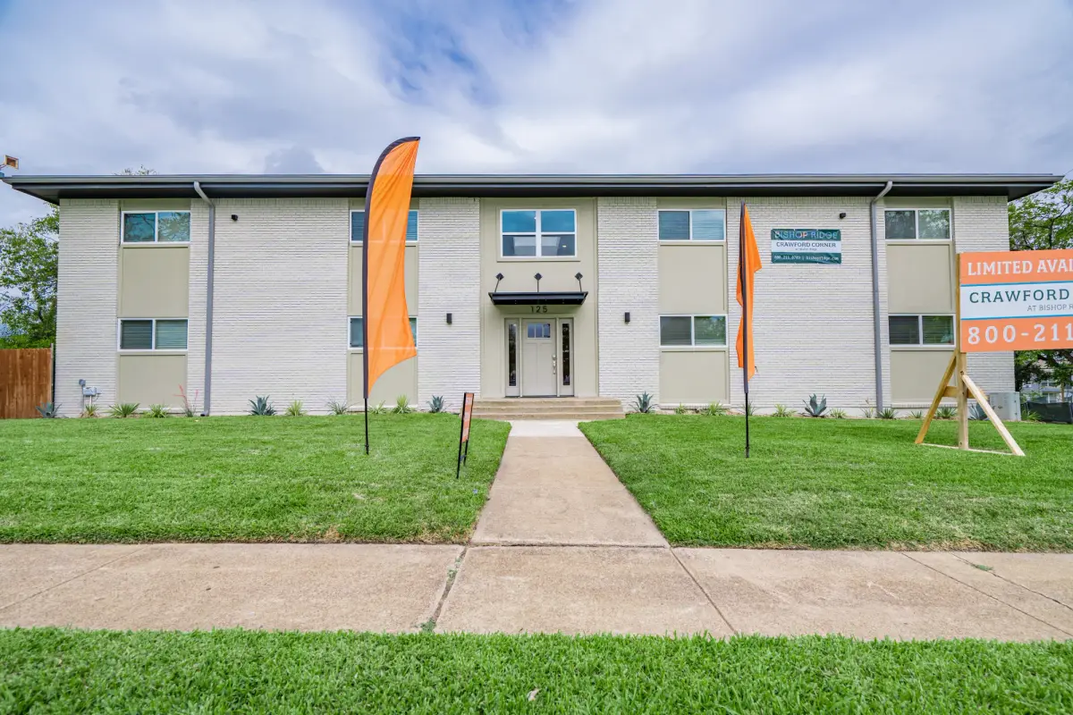 Two-story white-and-sage painted brick building with orange feather flags and a Crawford Corner sign on a landscaped lawn