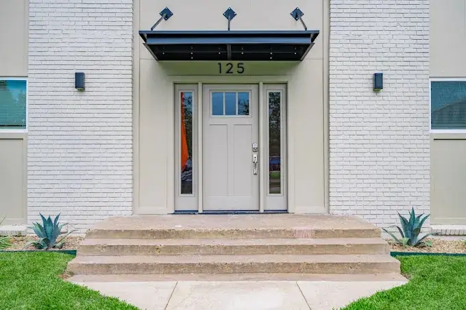 Building entry with a craftsman-style front door numbered 125, a black awning, and agave plantings on white-painted brick