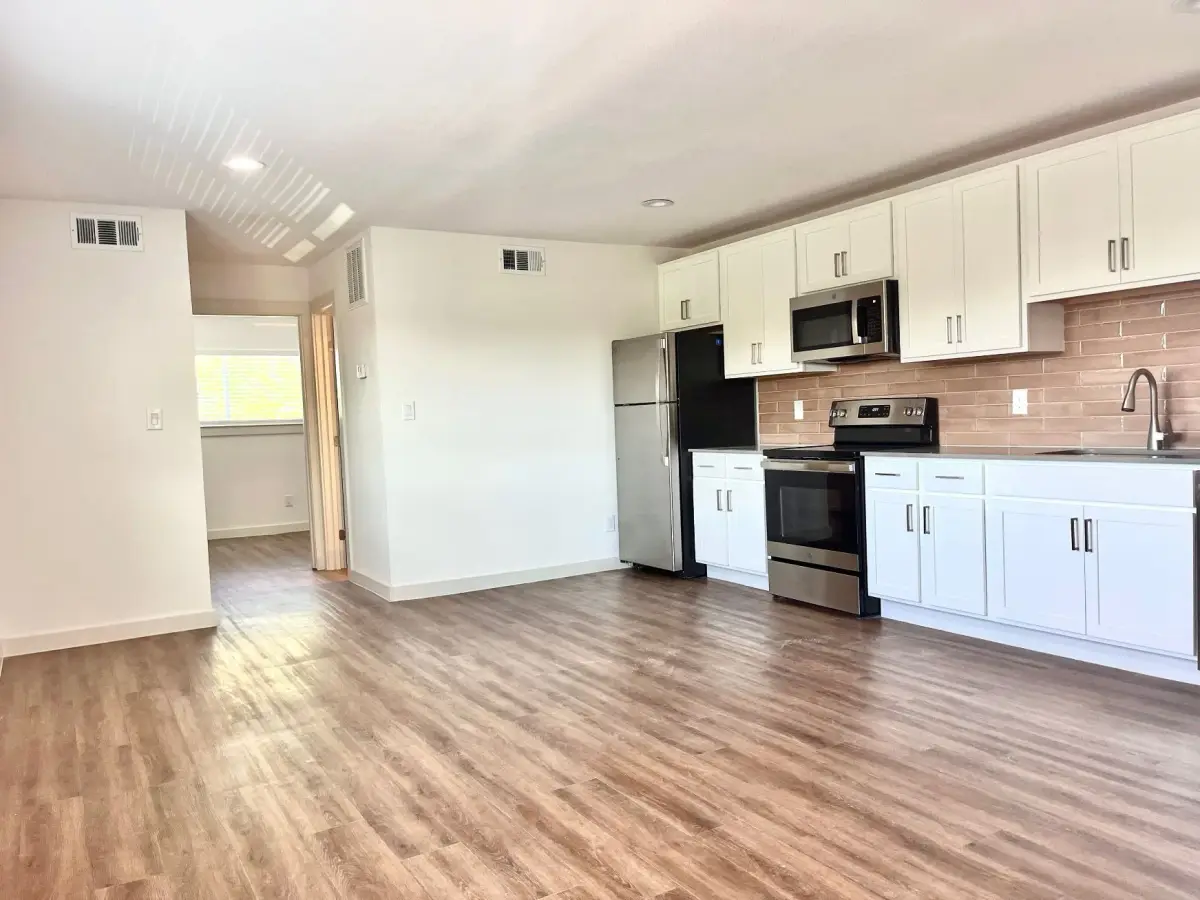 Open living and kitchen area with white cabinets, stainless appliances, and hardwood-style flooring