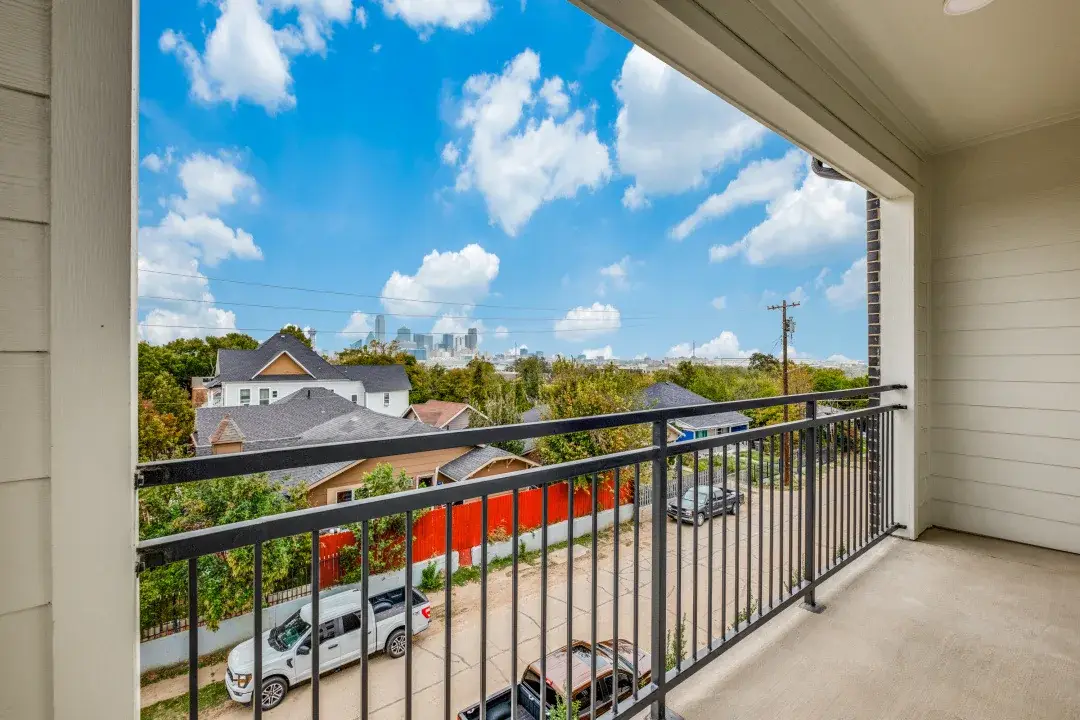 Private covered balcony with a black metal railing overlooking the neighborhood and the distant Dallas skyline