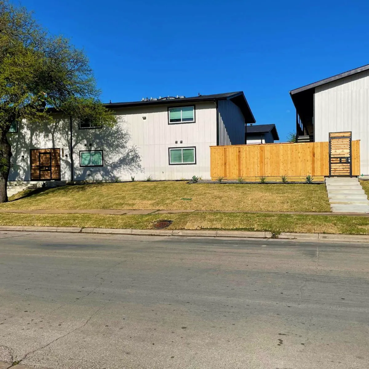 Street view of Hoskins 90's white two-story buildings joined by a cedar privacy fence with a gated walk-up entry