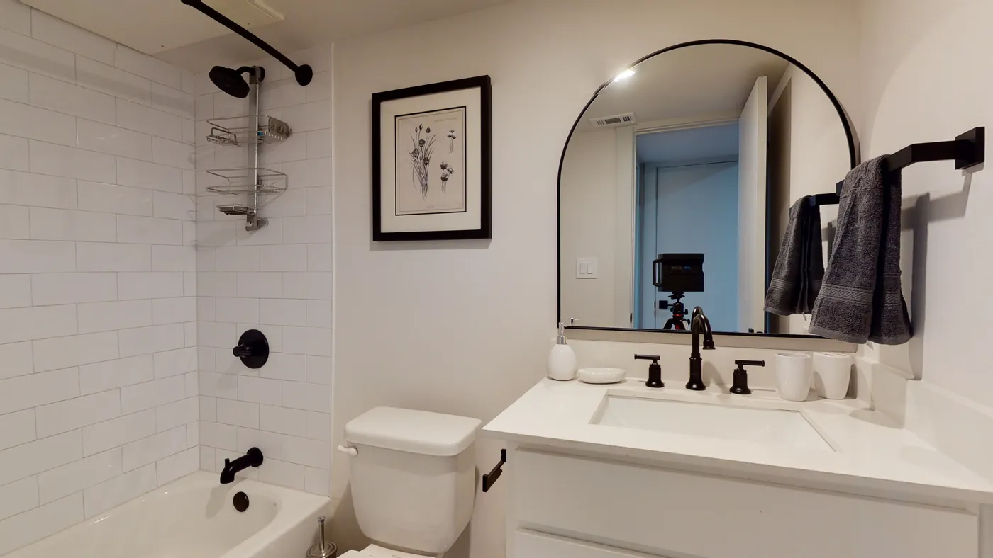 White subway-tile shower over the tub, black arched mirror and towel bar with gray towels, and a quartz-topped vanity
