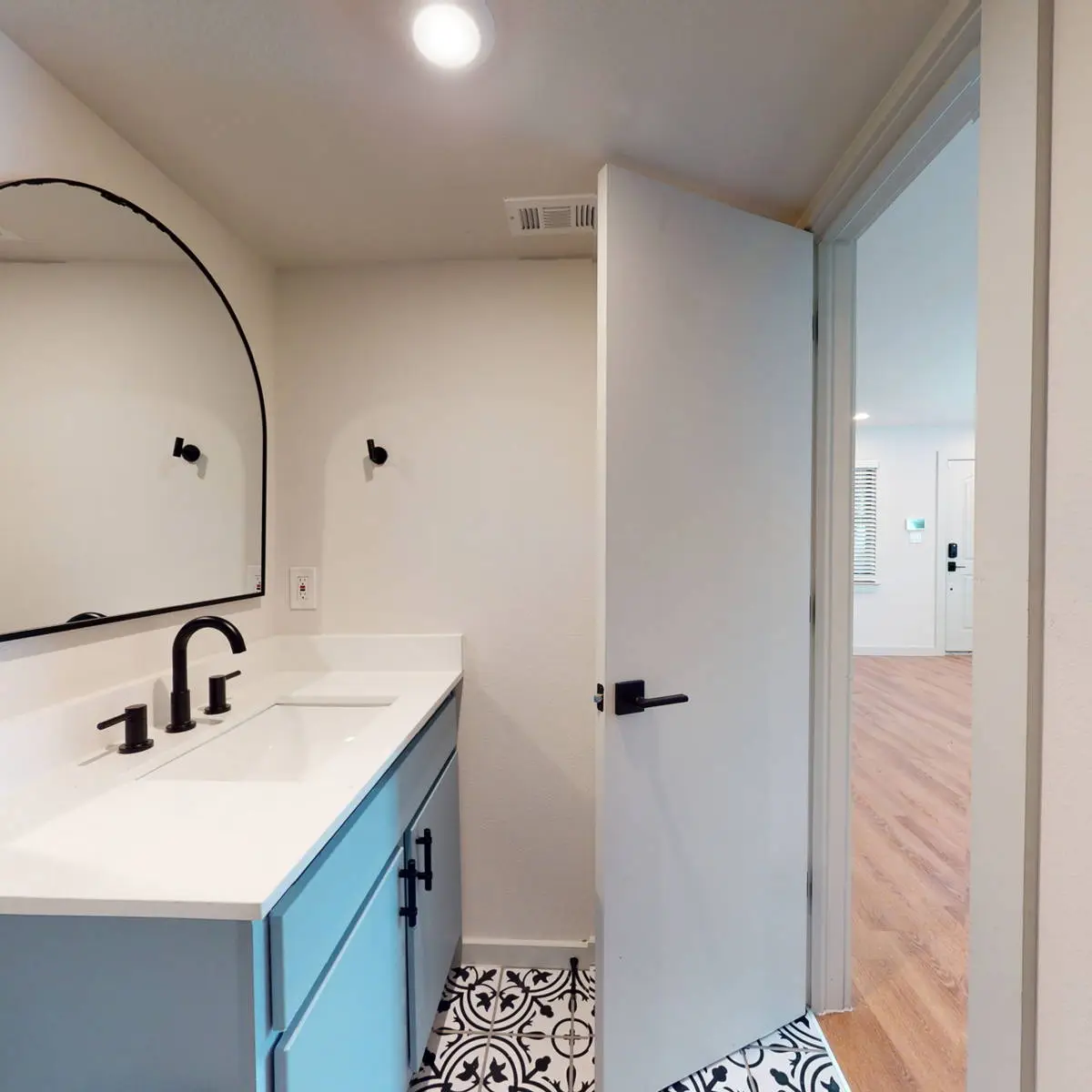 Bathroom with a blue vanity, white quartz top, black fixtures, arched mirror, and a black-and-white encaustic-tile floor