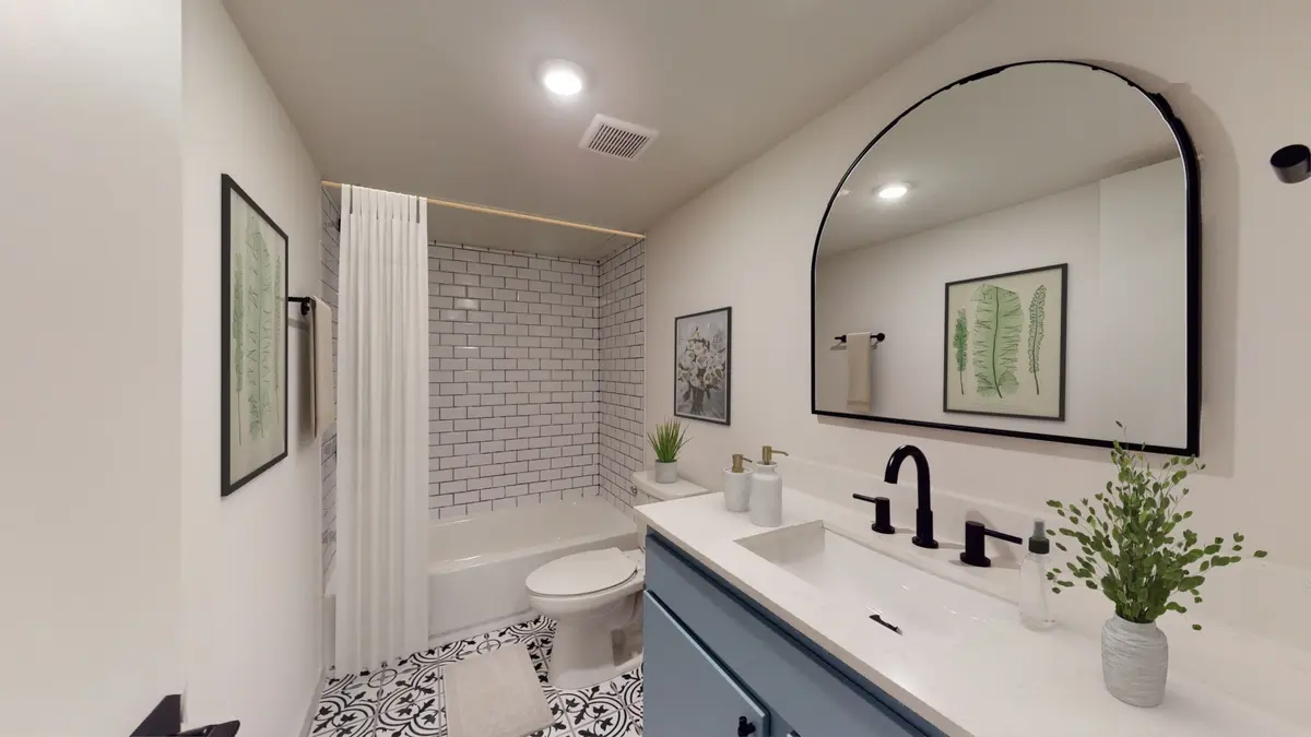 Bathroom with a blue vanity, arched black-framed mirror, a white subway-tile tub-and-shower, and an encaustic-tile floor