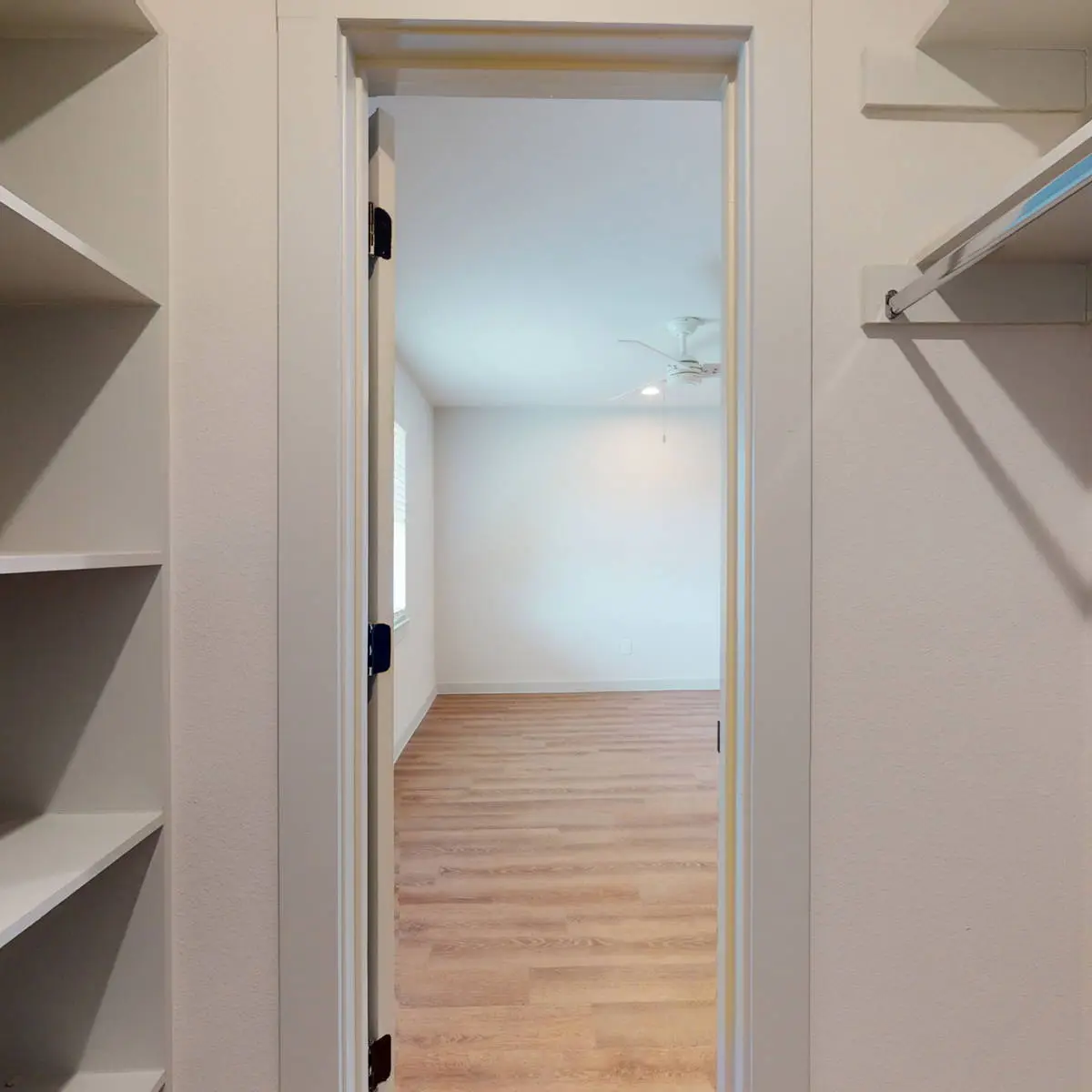 Walk-in closet with corner shelving and hanging rods opening to a bedroom