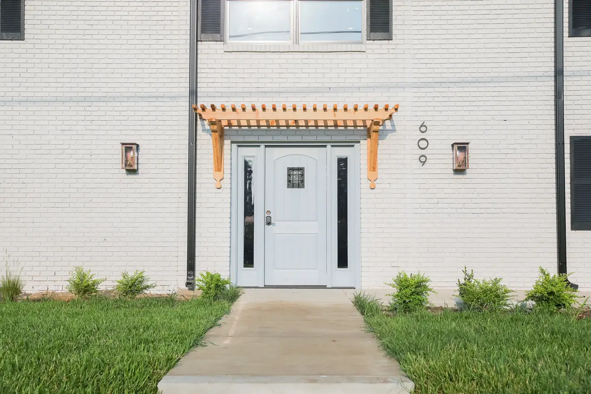 Entry door with a light-blue door, brass unit numerals, and a cedar pergola trellis on white-painted brick
