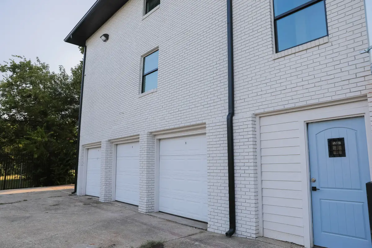 Exterior with three white garage doors and a blue side door on a white-painted brick building