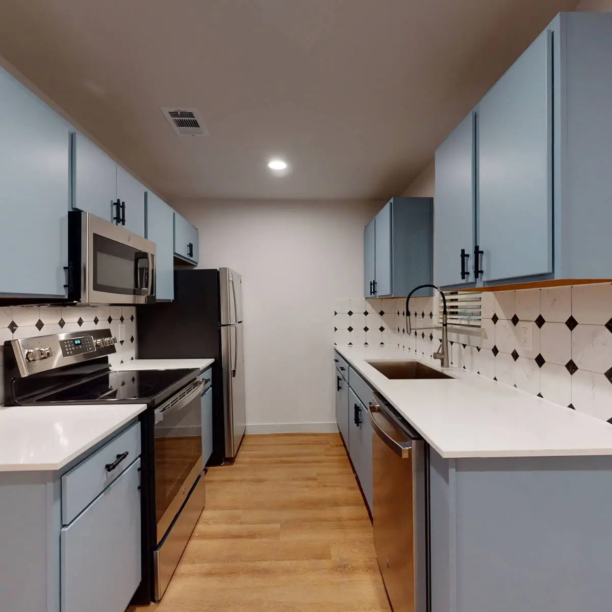 Galley kitchen with light-blue cabinets, white quartz counters, stainless appliances, and a black-diamond accent-tile backsplash