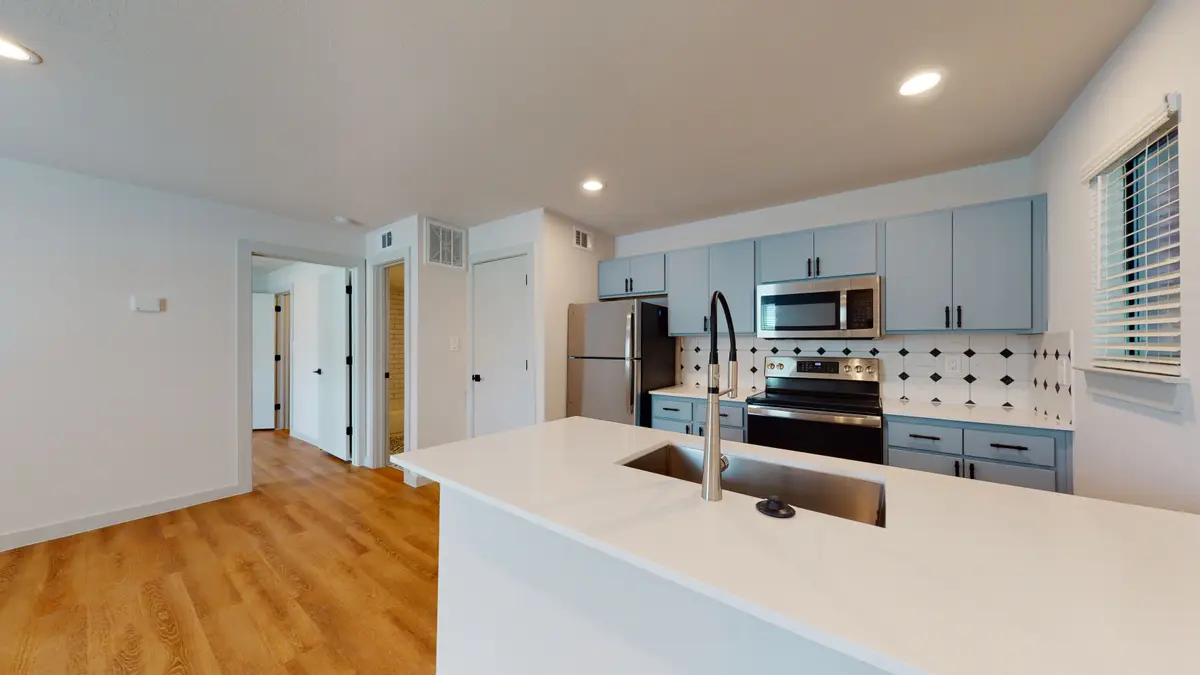 Open kitchen with light-blue cabinets, a white quartz peninsula with an undermount sink, and stainless appliances