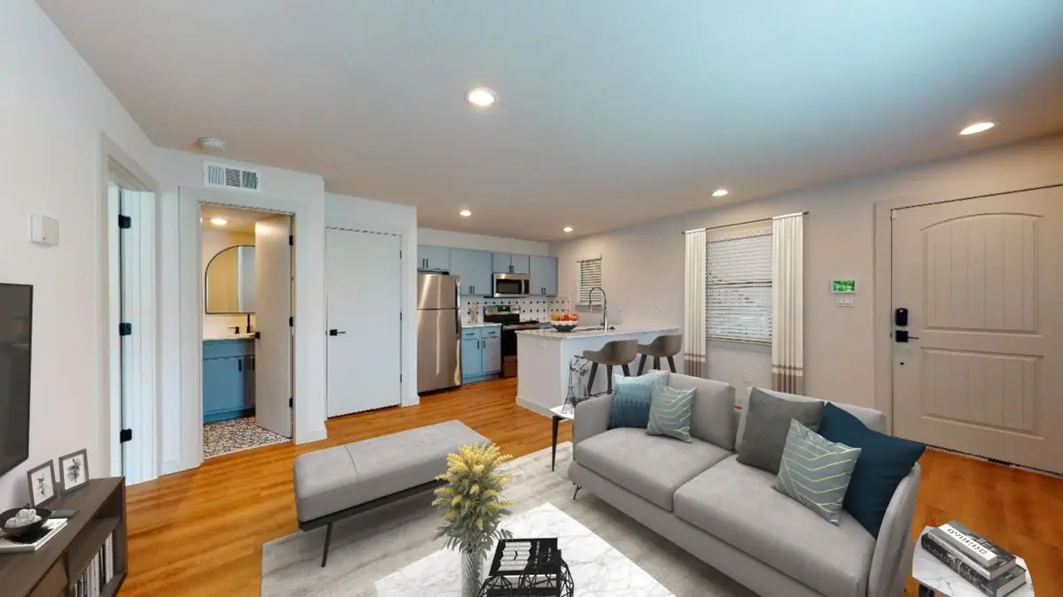 Living area with a sofa and ottoman opening to the kitchen and an entry door