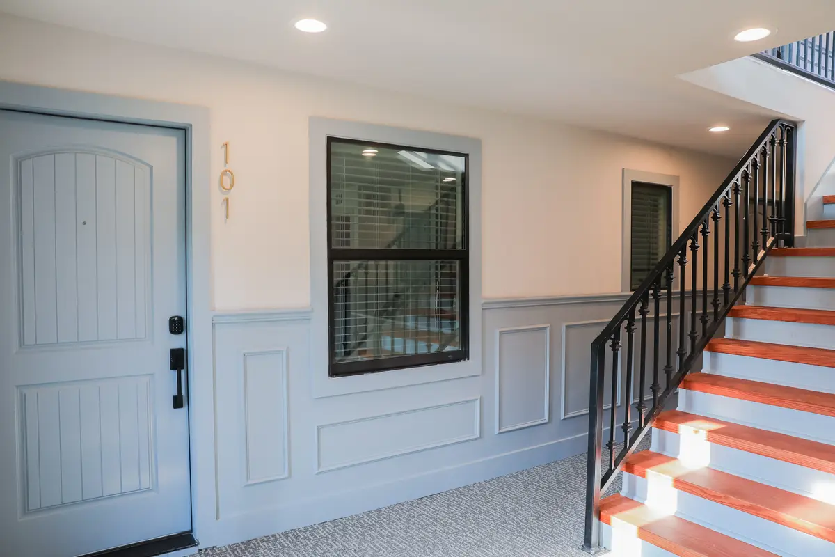 Interior stair landing with a blue unit door, wainscoting, and a black metal railing with cedar treads