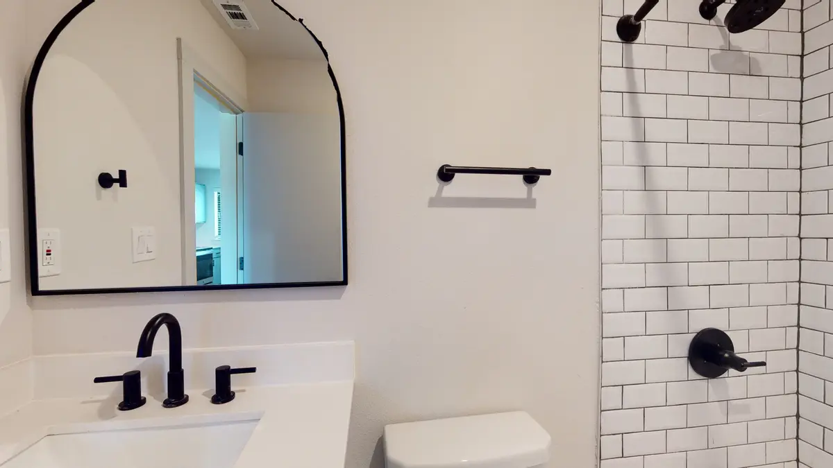 Bathroom with a white vanity, black fixtures, an arched black-framed mirror, and a white subway-tile shower