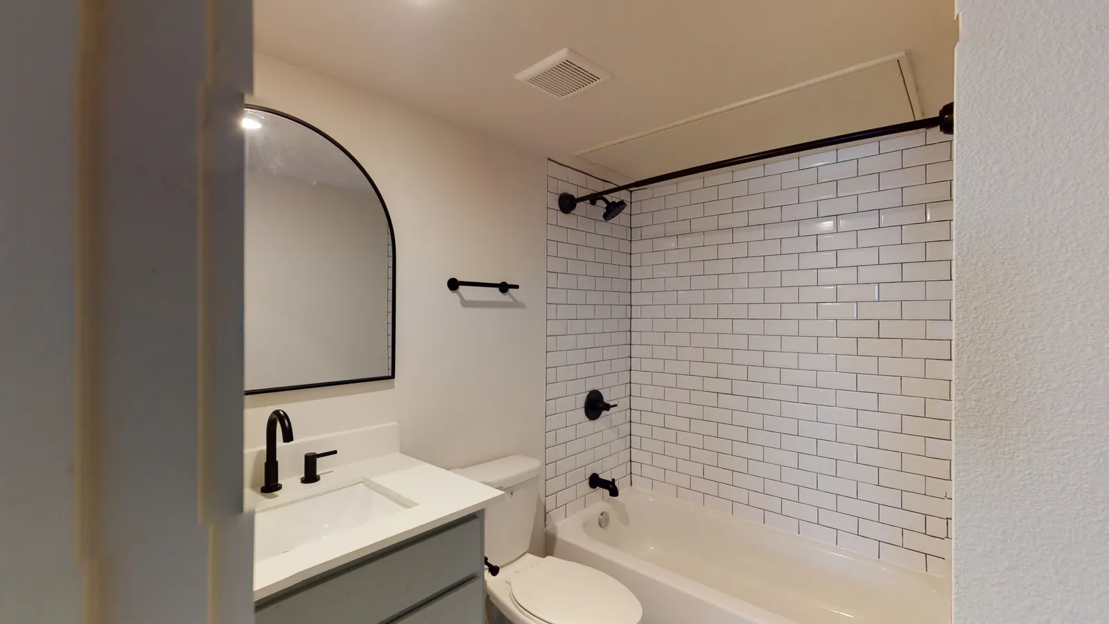 White subway-tile tub and shower with black fixtures beside the vanity and arched mirror