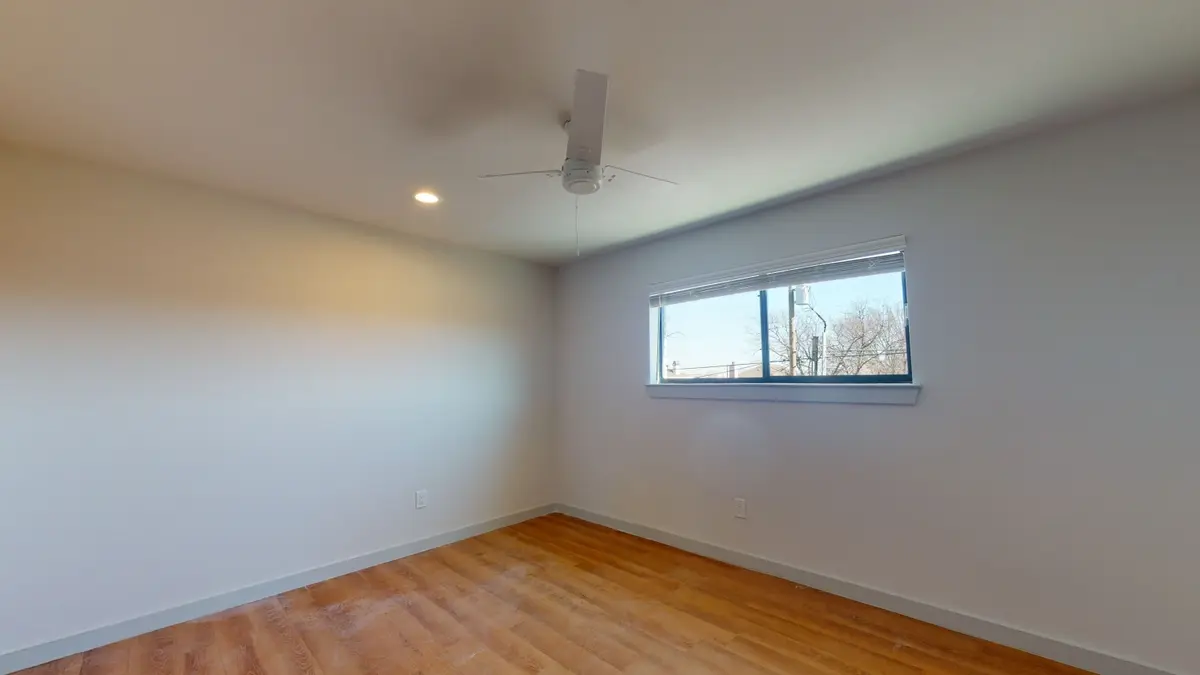 Bedroom with a gray accent wall, a ceiling fan, a window, and wood-look flooring