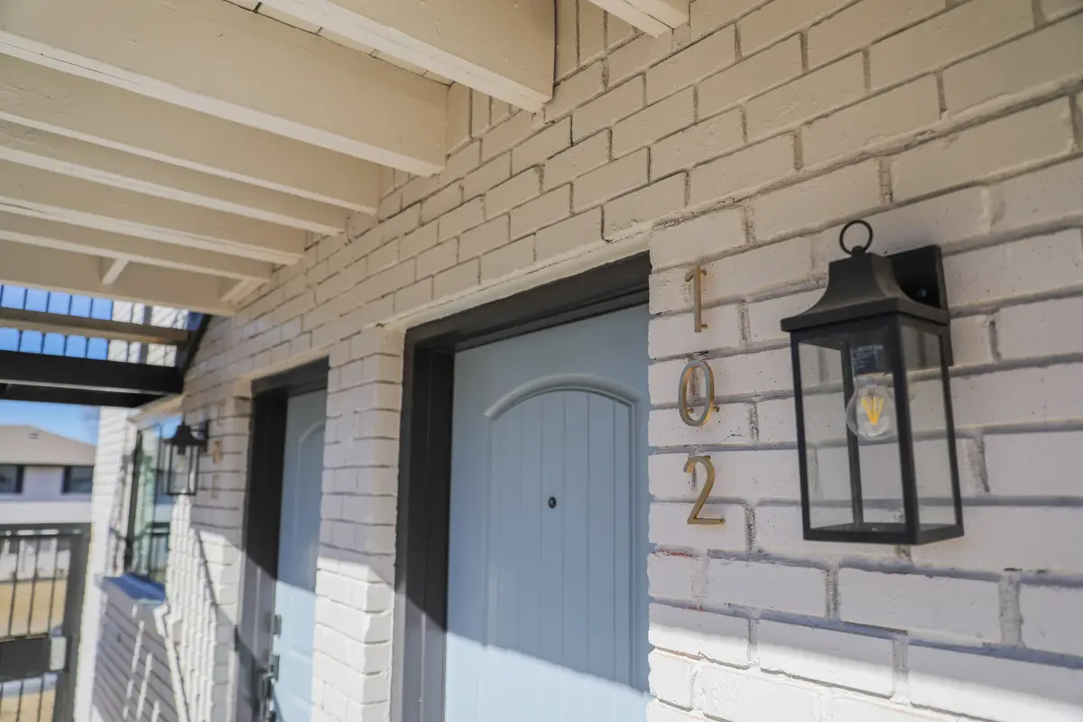 Unit entry with a light-blue door, brass numerals, and a black lantern sconce on white-painted brick