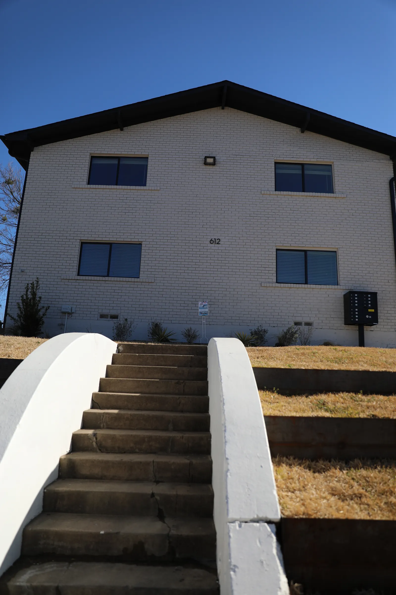Front elevation of the two-story white brick building above concrete steps climbing the landscaped rise