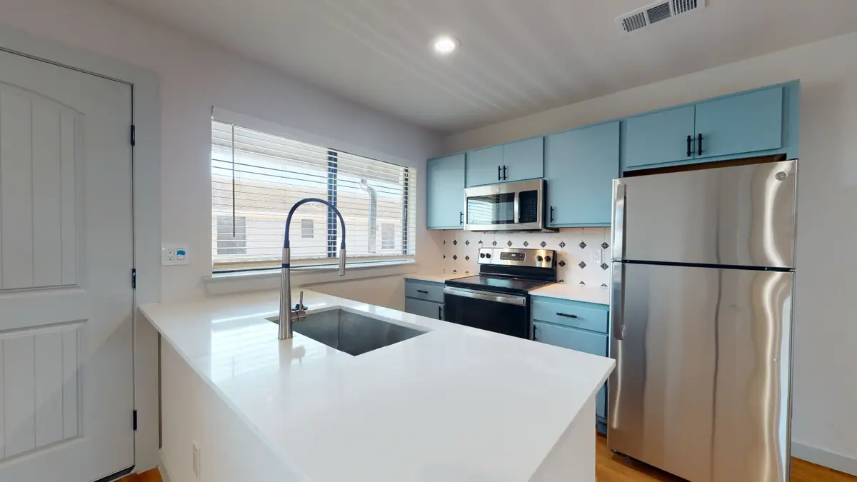 Kitchen peninsula with teal cabinets, white quartz, an undermount sink, and a white diamond-accent tile backsplash