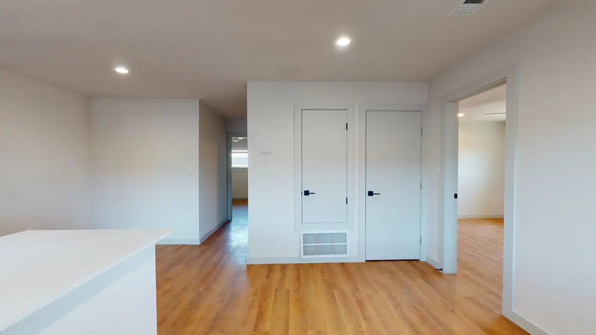 Living area beside the kitchen peninsula with closet and utility doors and wood-look flooring
