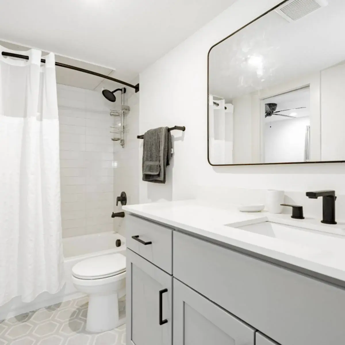 Bathroom with a gray vanity, white vanity top, black fixtures, framed mirror, and a tiled tub-and-shower