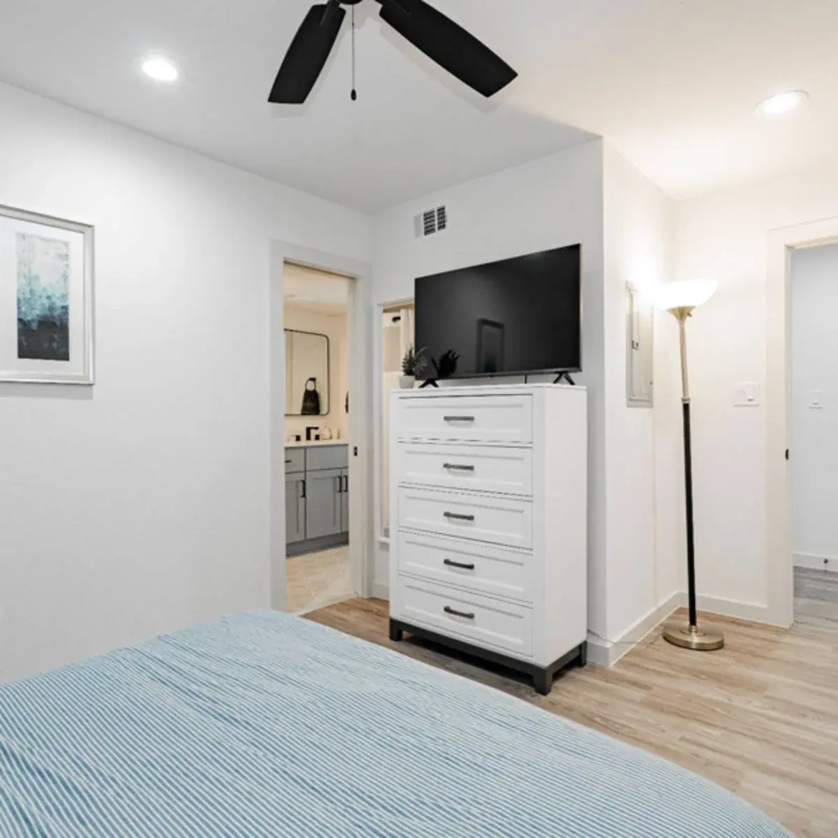 Bedroom with a dresser and TV, ceiling fan, and a doorway to the ensuite bathroom