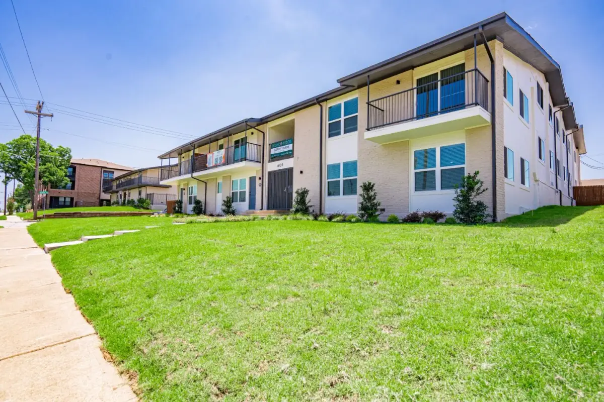 Two-story exterior of Kirby Yards with tan brick, white accents, private balconies, and a wide lawn