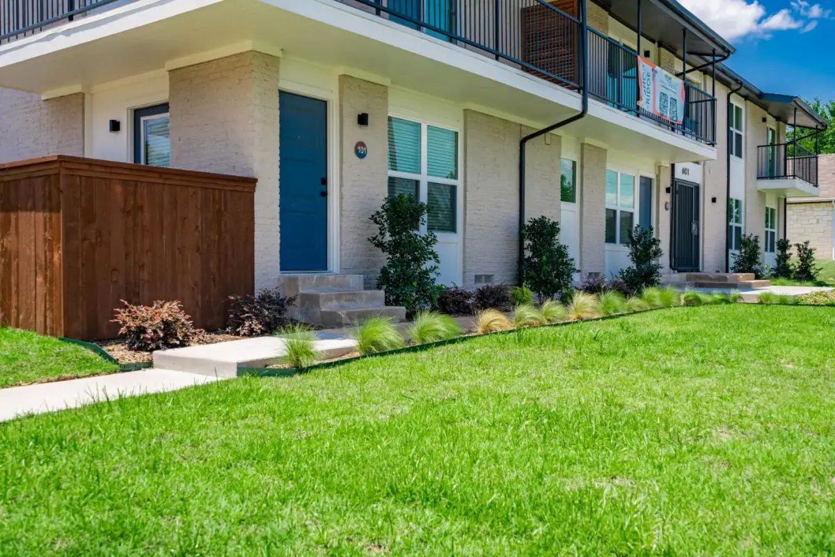 Ground-floor unit entries with blue doors, tan brick, and landscaped grasses along a walkway