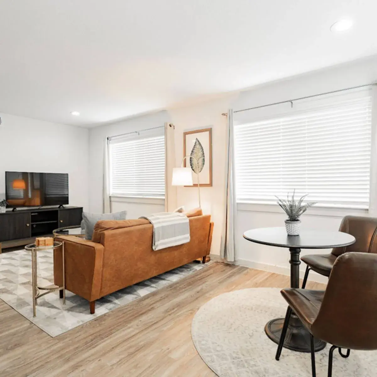 Open living and dining space with a tan sofa, media console, and a bistro table by the windows