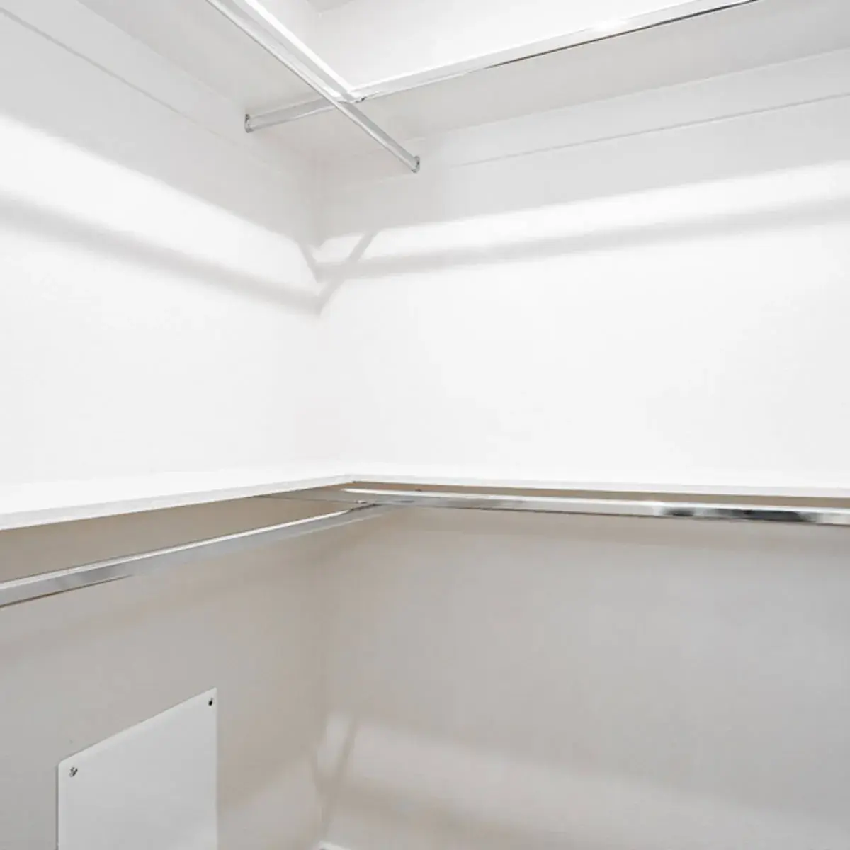White walk-in closet with double chrome hanging rods and a wraparound top shelf on two walls