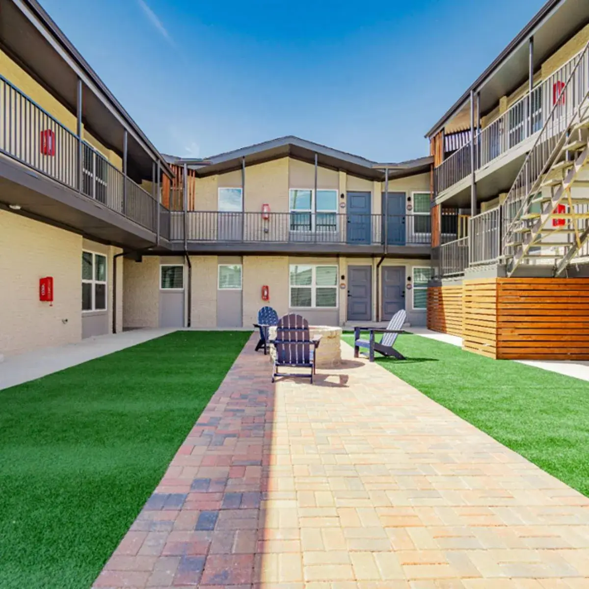 U-shaped courtyard with turf panels flanking a brick paver path to a stone fire pit ringed by Adirondack chairs