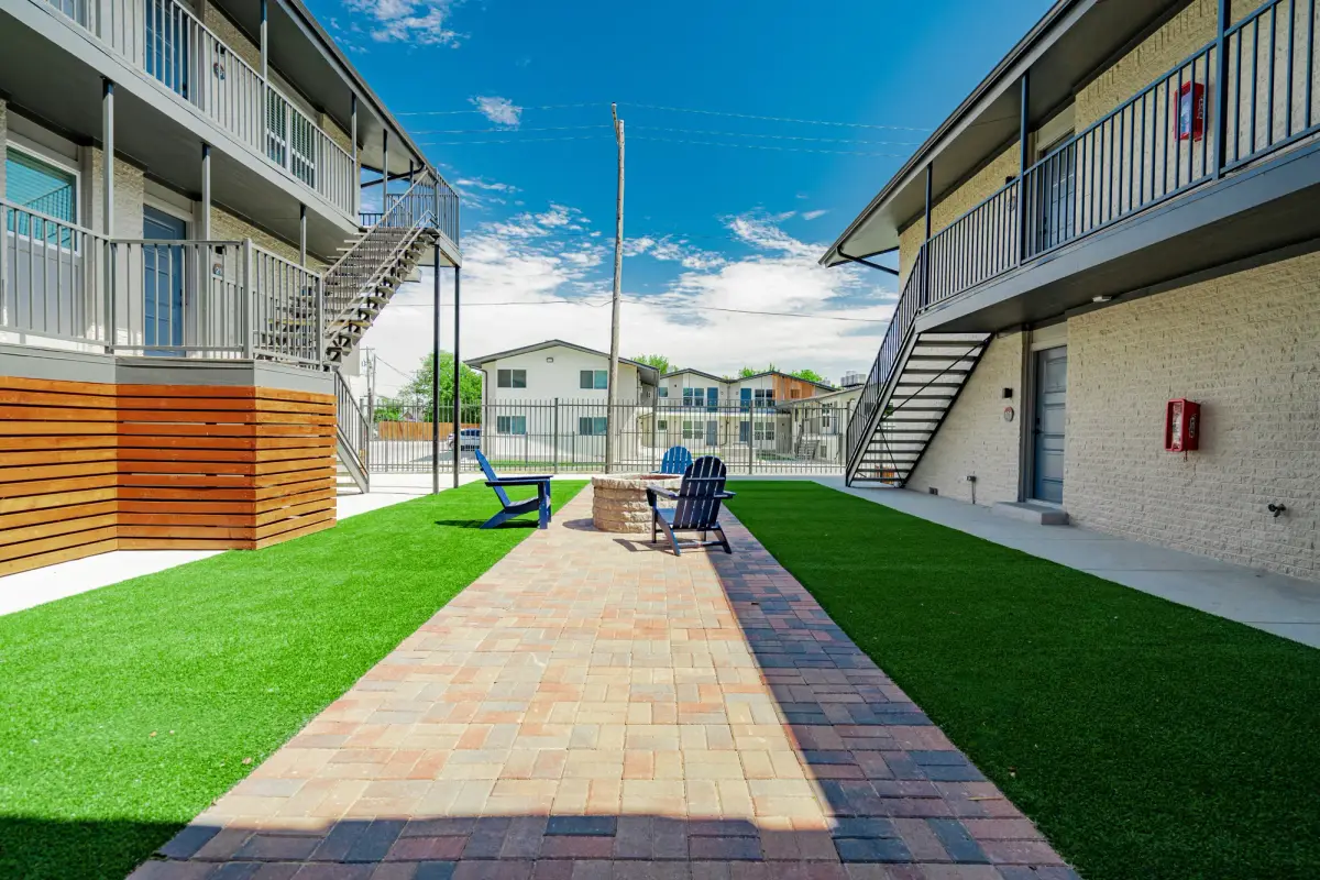 Paver walkway between twin turf lanes runs the courtyard's length, past fire-pit seating and cedar-wrapped stairs