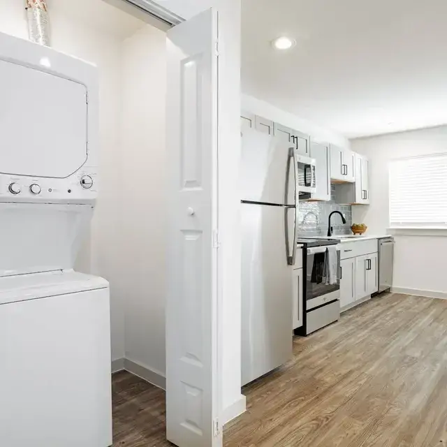 White stacked washer-dryer in a bifold-door closet beside the kitchen's white cabinets and stainless fridge