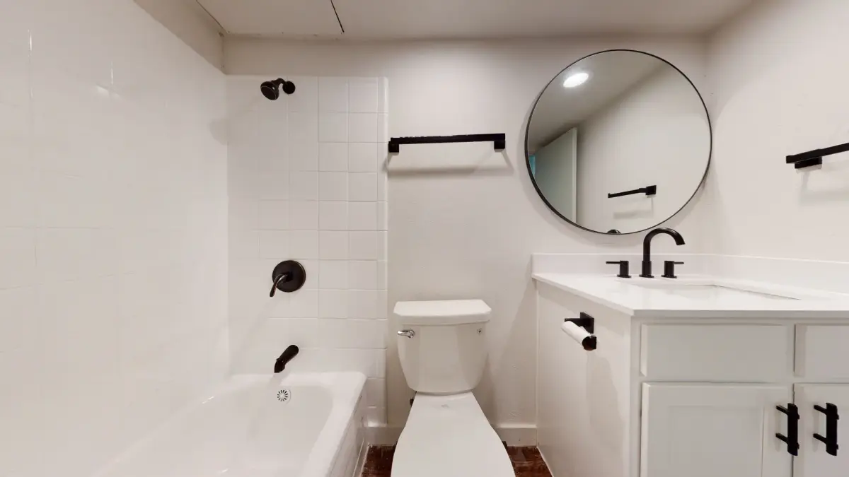 Bathroom with a white vanity, black fixtures, a round black-framed mirror, and a white-tile tub-and-shower