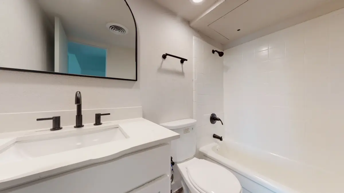 Bathroom with a white vanity, granite, black fixtures, an arched black-framed mirror, and a white-tile tub-and-shower