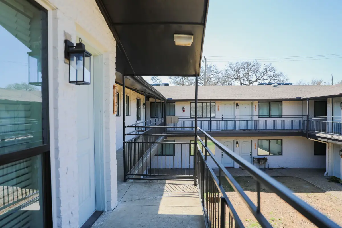 Upper exterior balcony walkway with black railings and a lantern sconce overlooking the courtyard