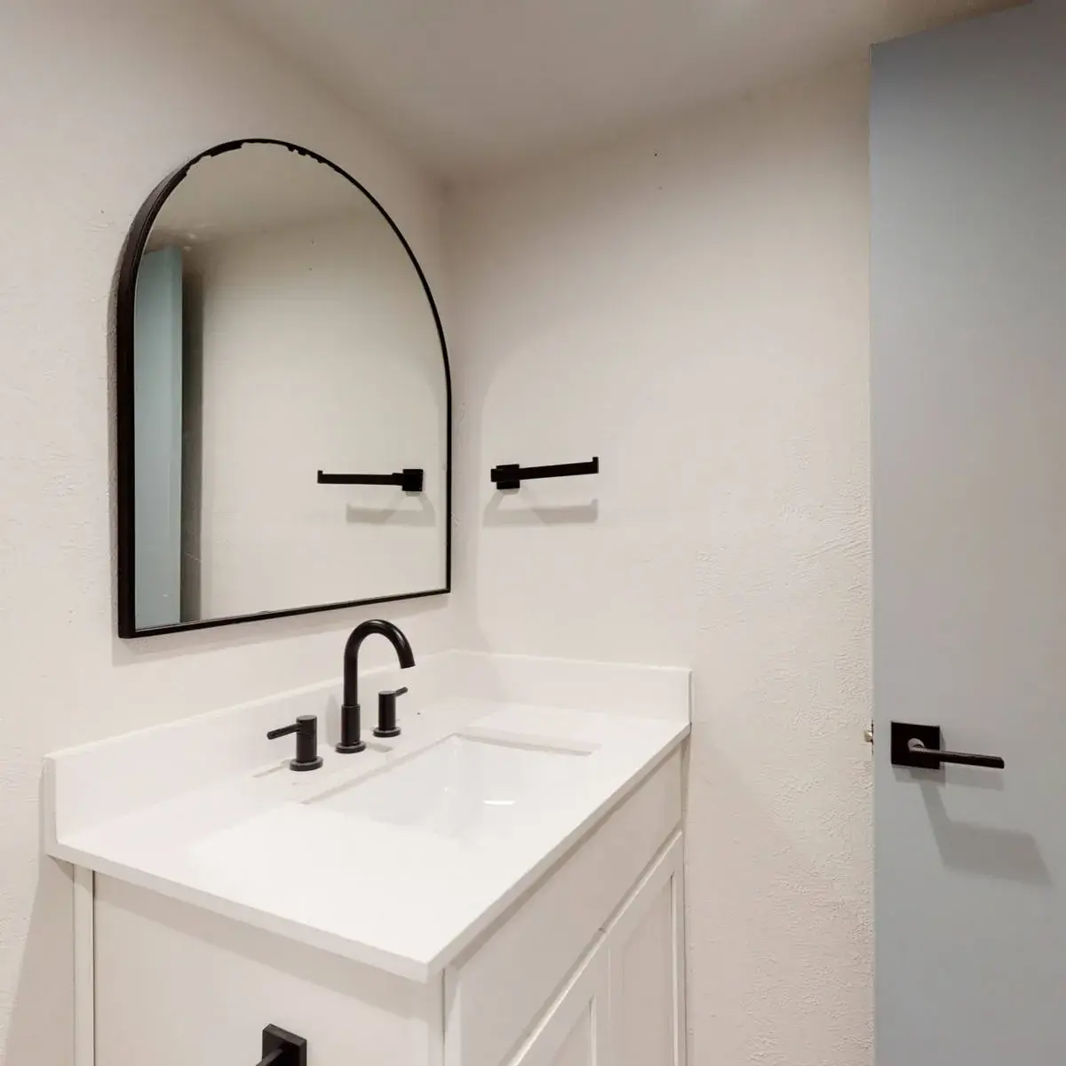Bathroom with a white vanity, white top, black fixtures, and an arched black-framed mirror