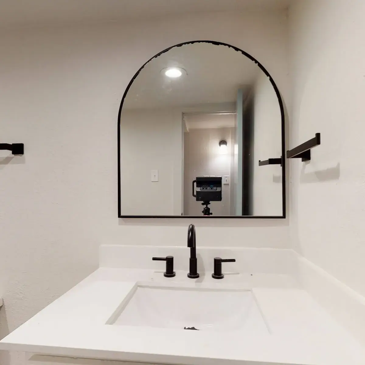 Bathroom with a white vanity, white countertop, black fixtures, and an arched black-framed mirror