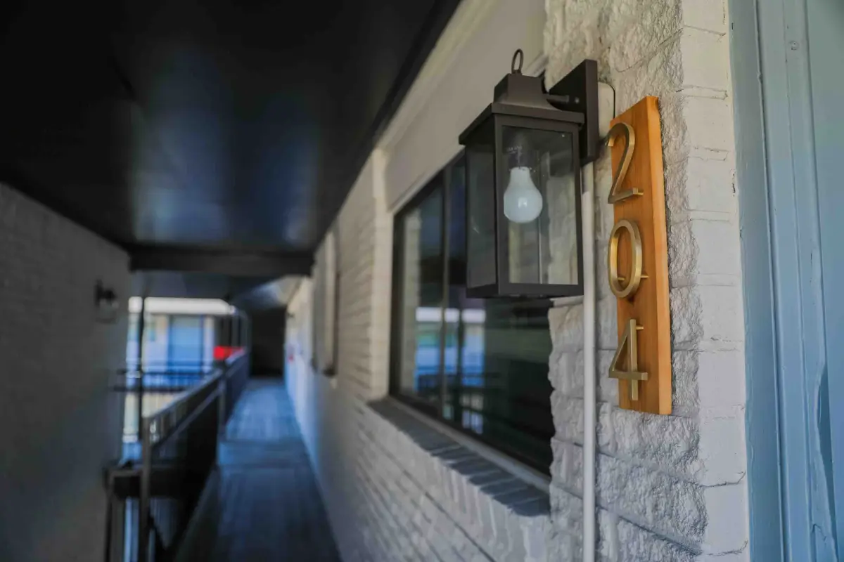 Exterior walkway detail with a black lantern sconce and brass unit numbers mounted on white-painted brick