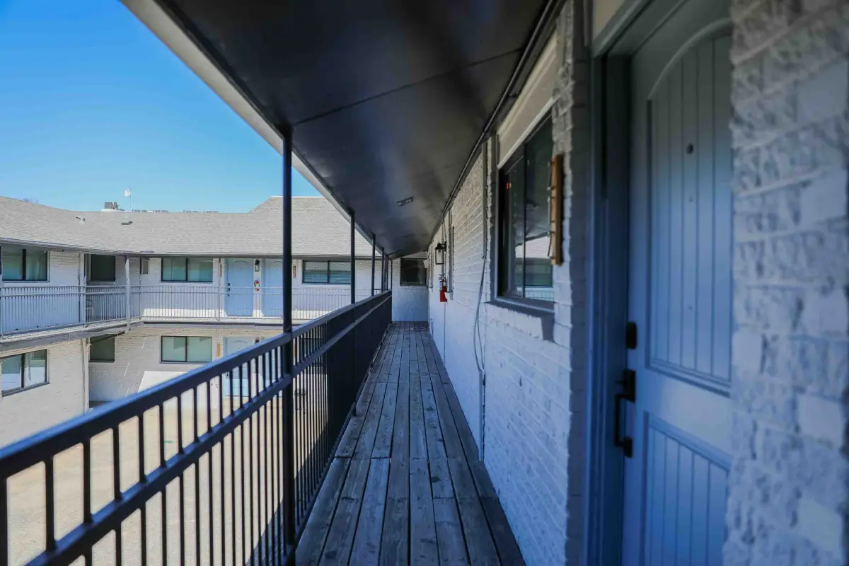 Upper exterior balcony walkway with a wood-plank deck and black railing overlooking the courtyard