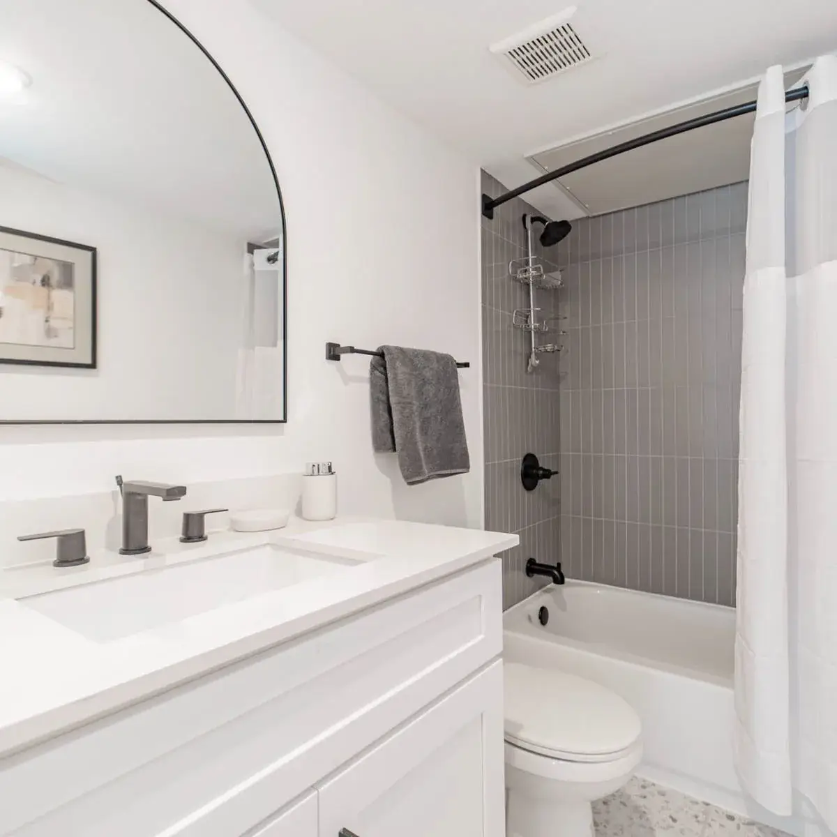Bathroom with a white vanity, black fixtures, an arched black-framed mirror, and a gray vertical-tile tub-and-shower