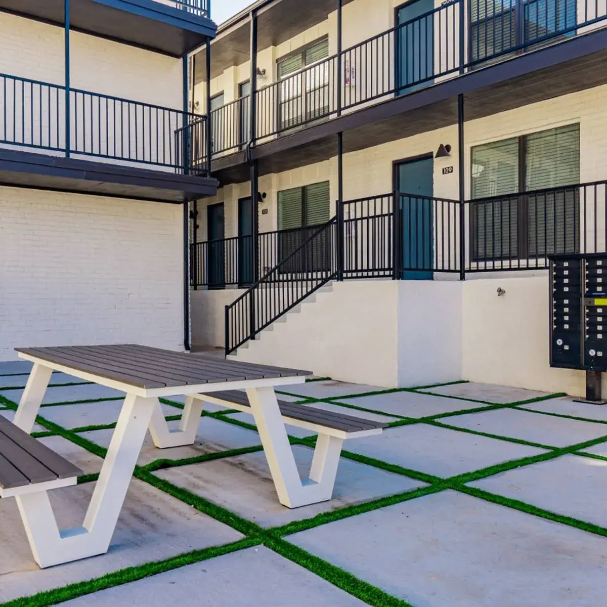 Courtyard with a picnic table, a raised patio with stairs, and cluster mailboxes against the white-painted building