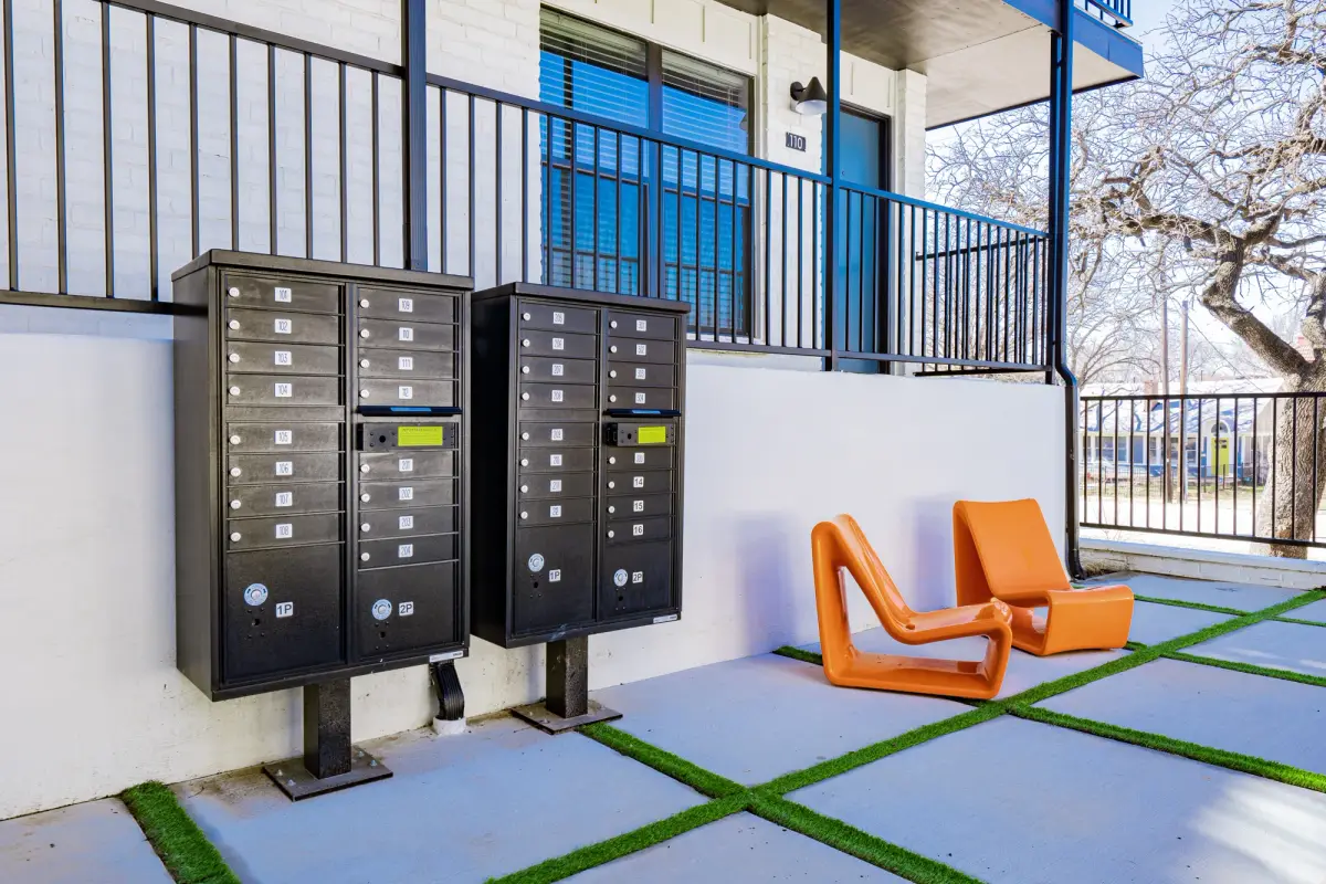 Courtyard seating area with cluster mailboxes and orange molded chairs on a paver-and-turf grid