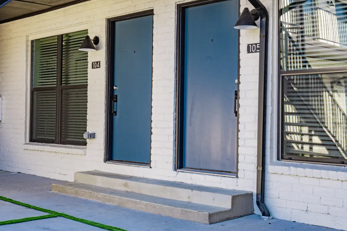 Ground-floor unit entries with blue doors, black sconces, and concrete steps on white-painted brick